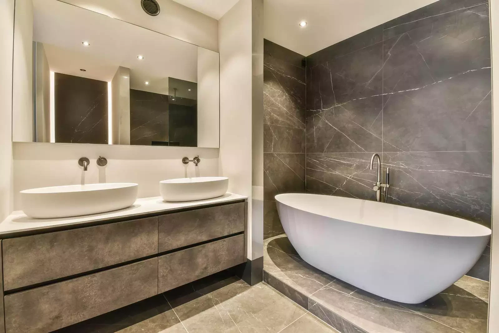 The interior of a marble bathroom with a ceramic bathtub and a double sink in a cozy house