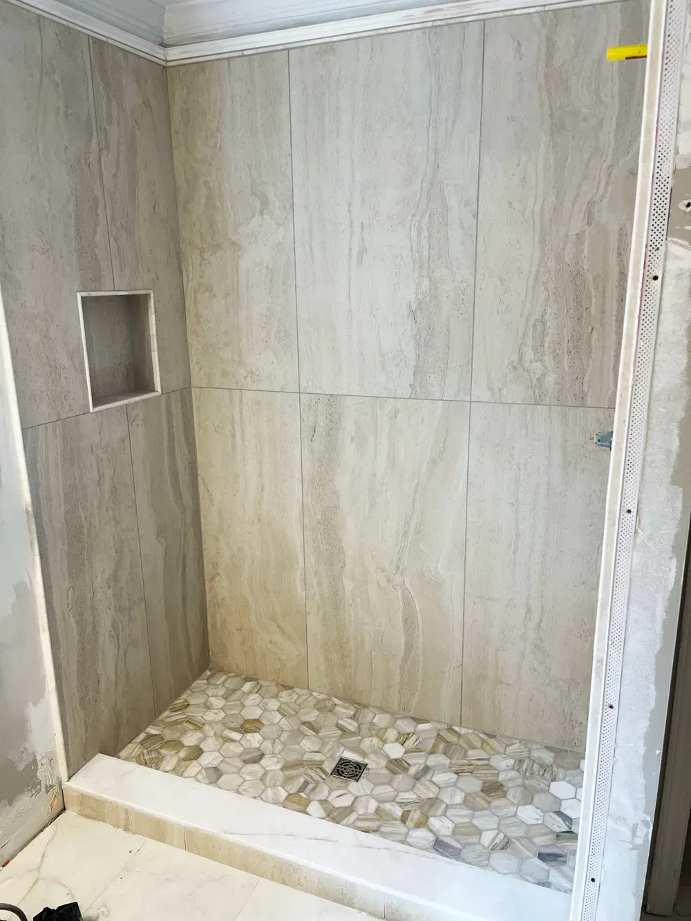 Unfinished bathroom shower with tiled walls and pebble floor